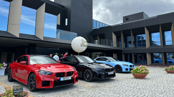 Três BMW M2, um vermelho, um preto e um azul à porta de um hotel.